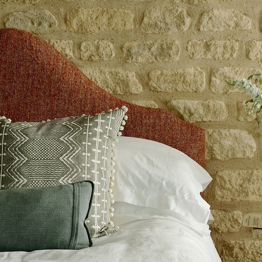 custom headboard on cotswold stone wall with bedspread and patterned cushions on top